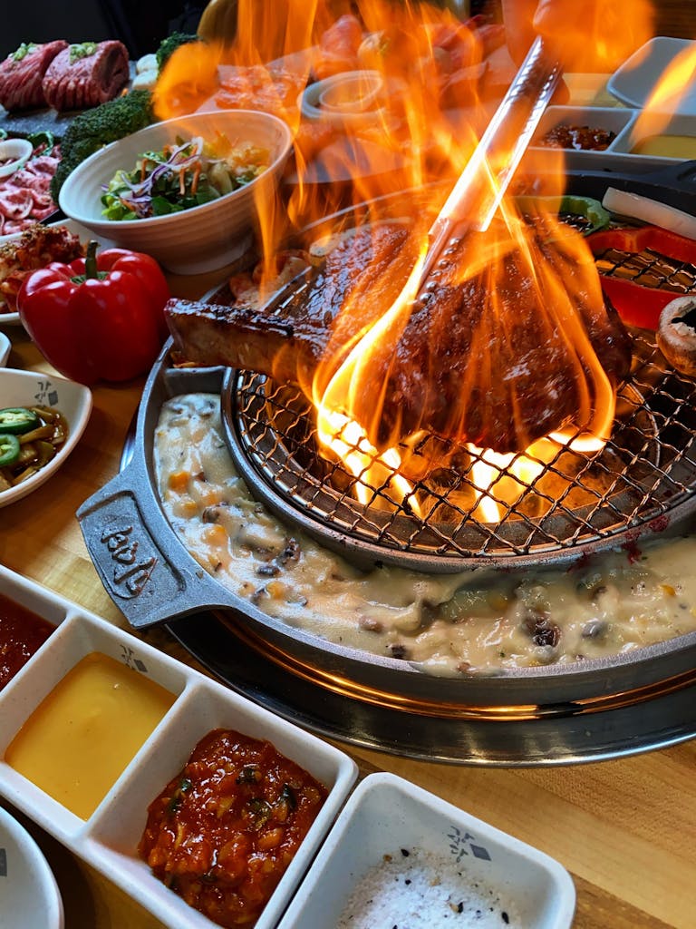 Delicious grilled steak with flames, surrounded by diverse side dishes in a vibrant BBQ setting.